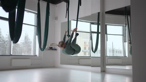 Young-smiling-woman-practice-in-aero-stretching-swing.-Aerial-flying-yoga-exercises-practice-in-green-hammock-in-fitness-club